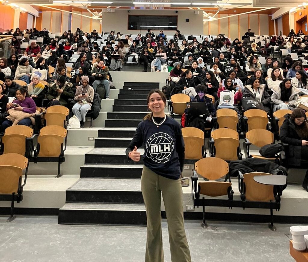 Person with thumbs up in front of a crowd at ElleHacks